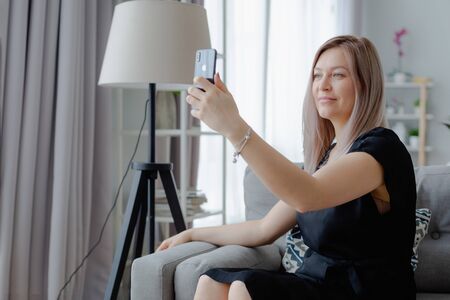 Blonde woman in a black dress sits taking a selfie