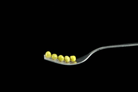 Fresh green peas on a silver fork, over black background.の写真素材