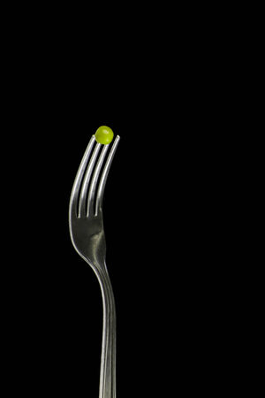 Fresh green peas on a silver fork, over blackbackground.