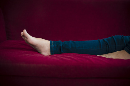Woman legs with wearing jeans while relaxing at movie theater or home at the red sofa, Relax and holiday concept, Bed time sleeping conceptの写真素材