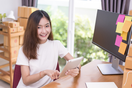 Asian woman using tablet with parcel boxes in delivery service theme. Part time and lifestyle conceptの写真素材