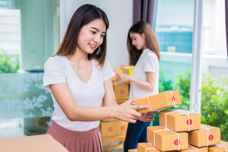 Two young Asian girl freelancers business owner working at home office and sorting parcel post box to delivery service to customer. Packaging order and Shopping online concept.の写真素材