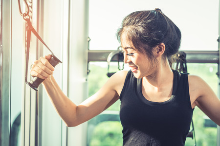 Asian young woman doing elastic rope exercises at cross fitness gym. Strength training and muscular...