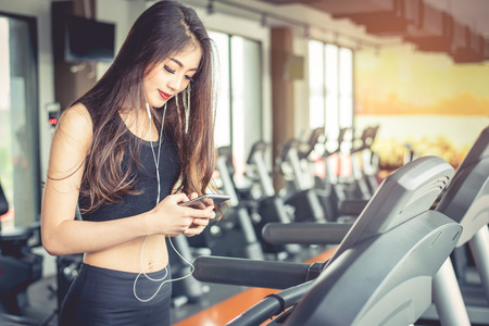 Asian woman using smart phone when workout or strength training at fitness gym on treadmill. Relax and Technology concept. Sports Exercise and Health care theme. Happy and Comfortable mood.の写真素材