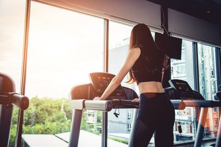 Asian sport woman walking or running on treadmill equipment in fitness workout gym. Sport and Beauty concept. Workout and Strength Training theme. Cardio and Diet themeの写真素材