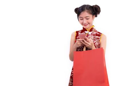 Young Asian beauty woman wearing cheongsam and using smart phone gesture in Chinese new year festival event on isolated white background. Technology and Holiday lifestyle concept. Qipao dress wearingの写真素材