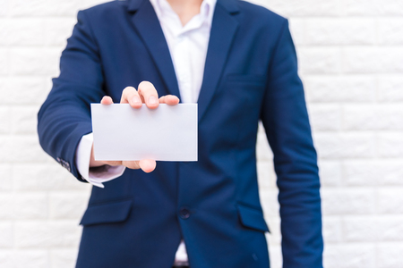 Business man showing white paper. Man  wearing blue suit and holding white blank card. Lifestyle and working concept. Business and object theme. Blank space in paper for insert text.の写真素材