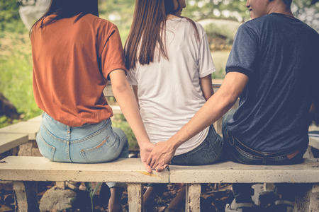 Boyfriend and another woman grab hands from behind together without sight of his girlfriend. Paramour and divorce concept. Social problem and cheating couples theme. Teen adult and University theme.の写真素材