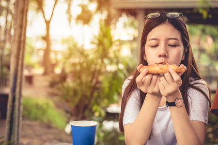 Asian woman enjoy eating slice of pizza at outdoors. Happiness after diet concept.  People lifestyle and Italian food concept. Nature background themeの写真素材