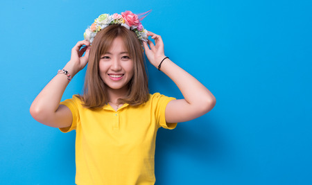 Beauty woman posing with flower hat in front of blue wall background. Summer and vintage concept. Happiness lifestyle and people portrait theme. Cute gesture and pastel tone.の写真素材