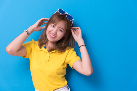 Beauty woman posing with sunglasses in front of blue wall background. Summer and vintage concept. Happiness lifestyle and people portrait theme. Cute and pastel tone.の写真素材