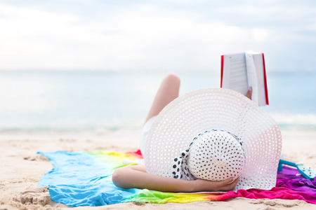 Asian woman sun bathing and reading books in holiday at beach. Beauty and Nature theme. Ocean and sea background. Woman day and relaxation themeの写真素材