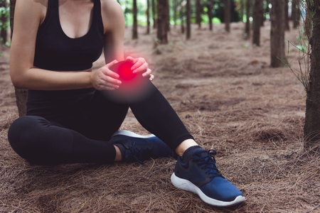 Sport woman injury at knee during jogging in forest. Pine woods background.  Medical and Healthcare concept. Nature and People theme. Lifestyles theme. Red light spot useの写真素材