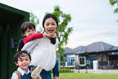 Single mom carrying and playing with her children in  garden with green wall background. People and Lifestyles concept. Happy family and Home sweet home theme. Outdoors and nature theme.の写真素材
