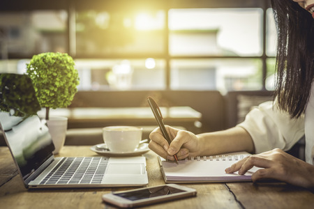 Close up of woman hand writing business project planning in notebook with laptop and smart phone at...