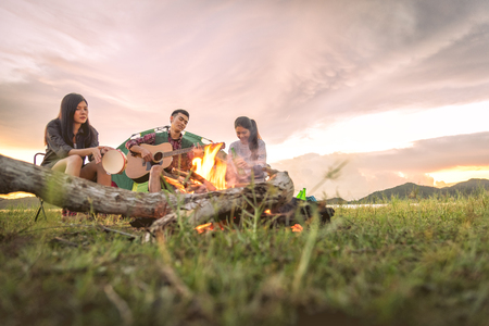 Group of travelers camping and doing picnic and playing music together. Mountain and lake background. People and lifestyle. Outdoors activity and leisure theme. Backpacker and Hiker. Dawn and twilightの写真素材