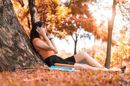 Asian beauty woman listen to the music in park. People lifestyles and Entertainment concept. Relaxation and Vacation concept. Autumn and fall seasonal theme.の写真素材