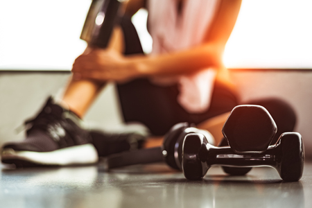 Close up dumbbells with woman exercise workout in gym fitness breaking relax after sport training with protein shake bottle background. Healthy lifestyle bodybuilding and athlete muscles lifestyle.の写真素材