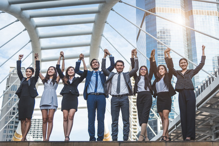 Portrait of successful group of business people at outdoor urban. Happy businessmen and businesswomen raising hand as team in satisfaction gesture. Successful group of people smiling after achievementの写真素材