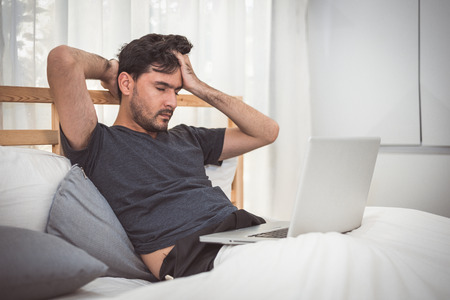Man stressed out from work with laptop in bedroom. Technology and lifestyle concept. Social issues and problem. Healthcare and Office syndrome. Economic downturn and Critical deadline crisis theme.の写真素材