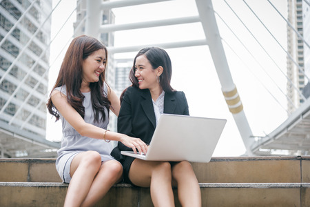Two businesswomen working on laptop computer with happy funny emotion. Teamwork cooperation meeting of business office employee technology collaboration. Marketing and finance community interactionの写真素材