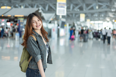 Happy beauty Asian woman traveling and holding suitcase in airport terminal with crowd people passengers background. People and Lifestyle concept. Journey around the world theme. Cheerful tourist girlの写真素材