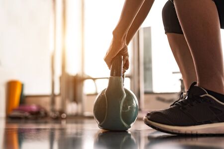 Close up of woman lifting kettlebell like dumbbells in fitness sport club gym training center with sport equipment near window background. Lifestyles and workout exercise for bodybuilding and healthyの写真素材