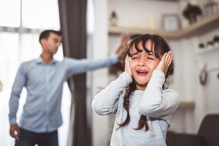 Little girl crying because of her parents quarreling. Girl abused with mother and father shouting and conflict angry background in home. Family dramatic scene, Family social issues problem concept.の写真素材