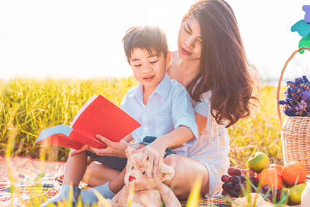 Little Asian boy and his mother reading books when doing picnic in meadow. Mother and son learning together. Celebrating in Mother day and appreciating concept. Summer people and lifestyle educationの写真素材