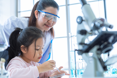 Scientist girl and teacher dropping solution substance liquid with pipette into test tube in lab classroom together. Education and Science. Micro and Nano technology. E-Healthcare and medical concept.の写真素材