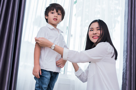 Young Asian mom dressed up son outfits for preparing go to school. Mother and son concept. Happy family and Home sweet home theme. Preschool and Back to school theme.の写真素材