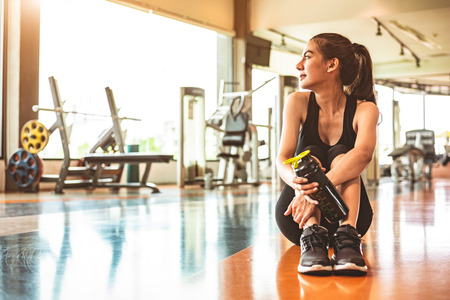 Sport woman relax resting after workout or exercise in fitness gym. Sitting and drinking protein shake or drinking water on floor. Strength training and Bodybuilder muscle theme. Warm and cool toneの写真素材
