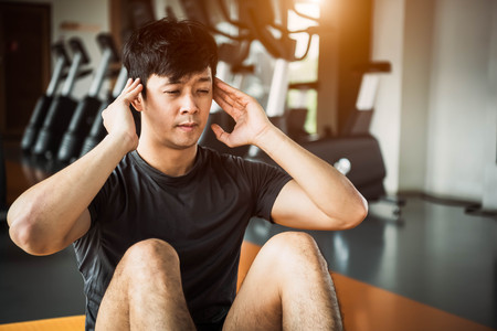 Asian sport man doing crunch or sit up posture on yoga mat in fitness gym at condominium with gym equipment background. Office working people lifestyles and Sport workout concept.の写真素材