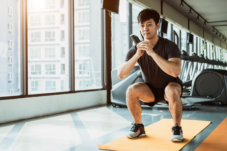 Sport man doing squat posture on yoga mat in fitness gym at condominium in urban. People lifestyles and Sport workout concept.の写真素材