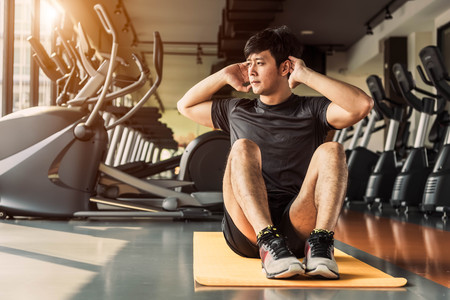Sport man doing crunch or sit up posture on yoga mat in fitness gym at condominium with gym equipment background. Office working people lifestyles and Sport workout concept.の写真素材