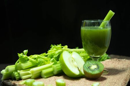 Blended mixed juice Celery and Kiwi and Green apple in welcome drink glass and bunch of fresh celery stalk on wooden table with leaves on black background. Food and ingredients  of healthy vegetable.の写真素材