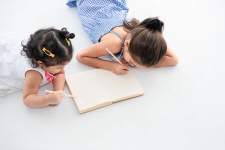 Top view of happy two sister drawing in sketch book together at home or nursery. People lifestyle...
