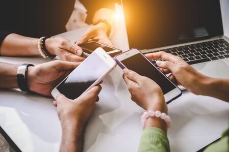 Group of young hipsters holding phone in hands at office. Friends having fun together with smartphones. Technology and communication concept. Black screen. Side view of teenager team using  phonesの写真素材