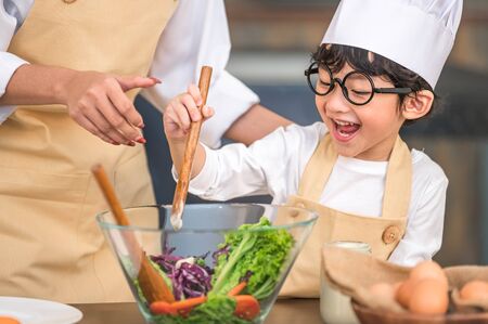 Cute little Asian happy boy interested in cooking with mother funny in home kitchen. People lifestyles and Family. Homemade food and ingredients concept. Two Thai people making diet saladの写真素材