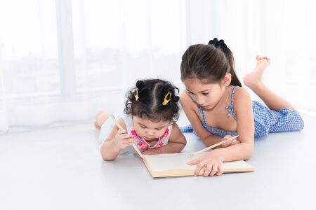 Happy two sister drawing in sketch book together at home or nursery. People lifestyle and kids play. Education and Children concept. Diverse ethnicity and ages. Back to school themeの写真素材