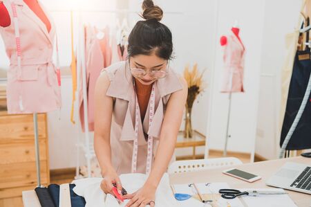 Attractive Asian female fashion designer working in home office workshop. Stylish fashionista woman creating new cloth design collection. Tailor and sewing. People lifestyle and occupation conceptの写真素材