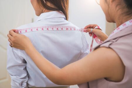 Dressmaker measuring female customer shoulder in sewing atelier workshop office. Tailor and fashion designer concept. Job and freelance occupation. Business people in clothing shopの写真素材