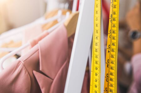 Closeup of measuring tape and line of fashion pastel pink colored woman shirts with wooden hangers in clothing shop.の写真素材