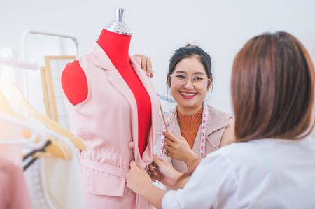 Attractive Asian female fashion designer working and recommending new design collection clothes on mannequin in clothing shop to customer. Tailor and sewing dressmaker. People lifestyle conceptの写真素材