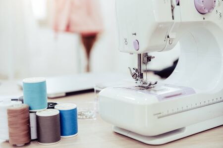Closeup of sewing machine with fashion designer showroom studio workshop background with new collection of pink pastel female clothes design. Tailor and sewing concept. Dressmaker modern room interiorの写真素材