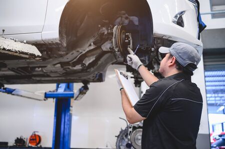 Asian male car technician car maintenance for customers according to specified vehicle maintenance checklist. Disk brake pad wear automotive repairing on vehicle. Safety inspection check serviceの写真素材