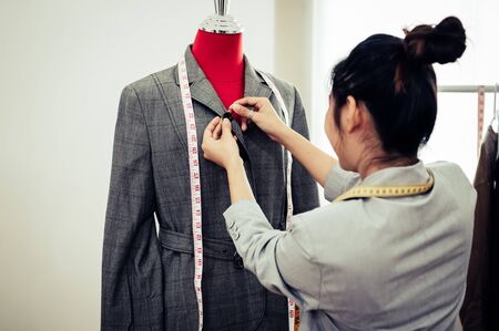 Asian female fashion designer girl making fit on the formal suit uniform clothes on mannequin model. Fashion designer stylish showroom. Sewing and tailor concept. Creative dressmaker stylist.の写真素材