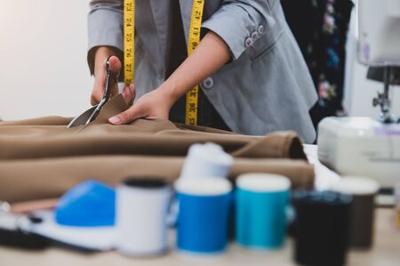 Dressmaker cutting dress fabric on sketch line with colorful thread foreground. Fashion designer tailor or sewer in workshop studio designing new collection clothes. Business owner and entrepreneurの写真素材