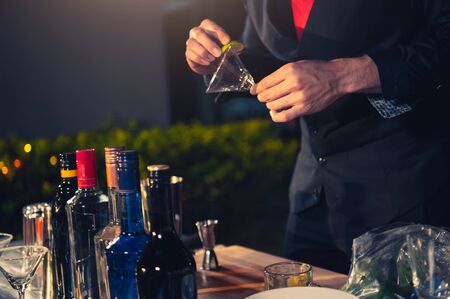 Professional bartender preparing fresh lime lemonade cocktail in drinking wine glass with ice at night bar clubbing counter. Occupation and people lifestyles concept. Outdoor backgroundの写真素材