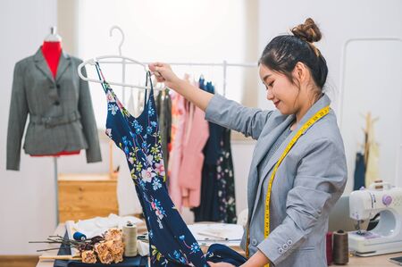 Asian female fashion designer girl making designing new beautiful blue dress clothes with hanger in studio. Fashion designer stylish showroom. Sewing and tailor concept. Creative dressmaker stylist.の写真素材